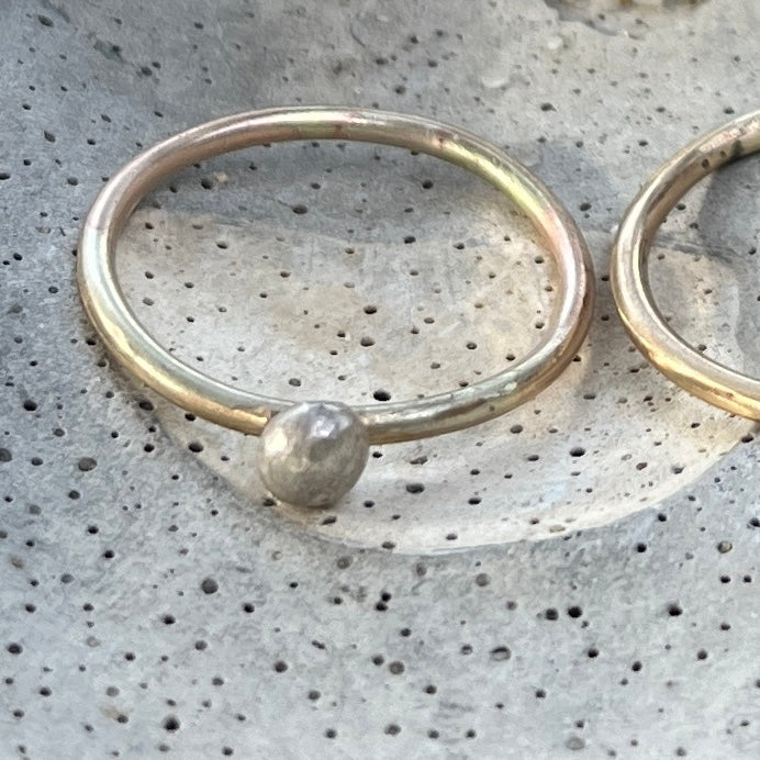 Daniella Farrell fine 9ct rose gold ring with a hand-shaped silver bobble, resting on speckled grey concrete