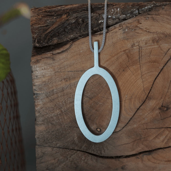 Kalinowski Cassini pendant, a hollow oval of powder blue anodised aluminium on a cord, hanging against weathered timber