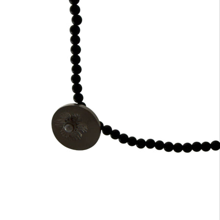 Close-up of a black beaded necklace with a button clasp on a light gray background