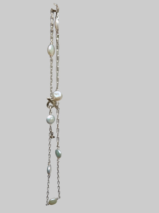 Pearl necklace with star and leaf pendants on a textured white surface