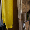 Yellow knitted garment and beige bag hanging on a wooden rack.