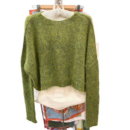 Green sweater on a hanger with a blurred background of clothing racks.