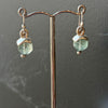 Green gemstone earrings on a stand against a dark background