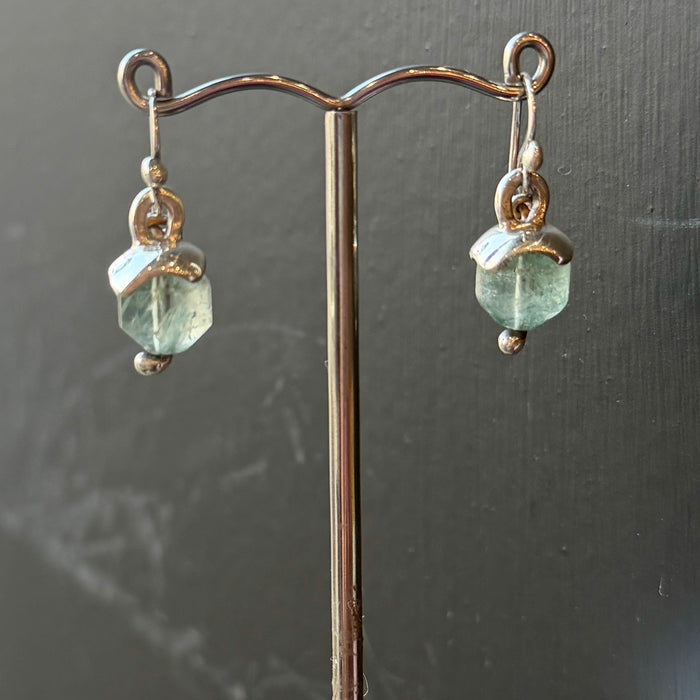 Green gemstone earrings on a stand against a dark background