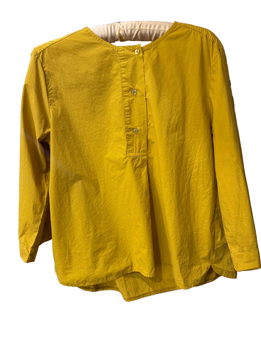 A mustard yellow long-sleeve linen shirt with a buttoned henley neckline, hanging on a wooden hanger in a shop setting.