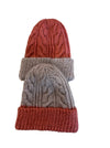 Two cable-knit beanie hats stacked on a patterned fabric surface. The top hat is coral red with a ribbed cuff, and the bottom hat is light taupe with a coral red ribbed cuff.