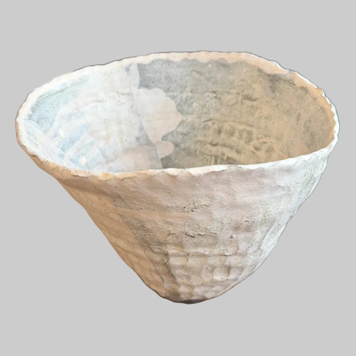 A handmade, textured ceramic planter pot with a wide, flared rim and a ribbed base, sitting on a rustic wooden table in what appears to be a vintage or antique shop.