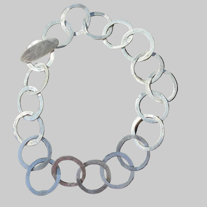 A chunky silver link bracelet made of thick, polished circular rings, displayed on a weathered wooden surface.