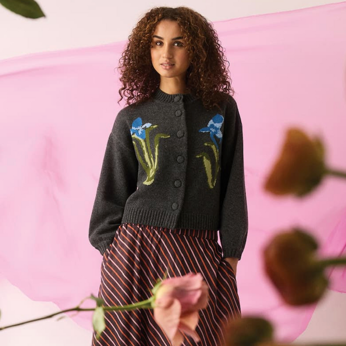 Woman wearing a dark gray cardigan with floral patterns against a pink background