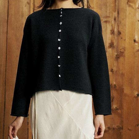 Person wearing a black cardigan with white buttons against a wooden background