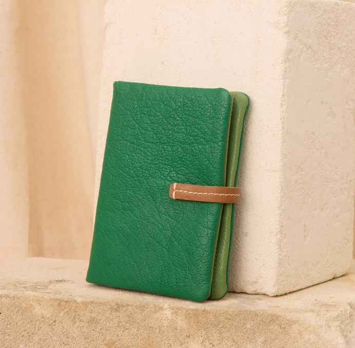 Green leather notebook with a strap on a beige surface