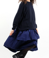 A person wearing a navy blue, tiered cotton skirt with an elasticated waist and side pockets, designed by Manuelle Guibal.