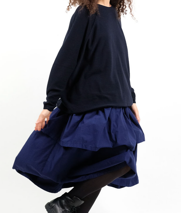 A person wearing a navy blue, tiered cotton skirt with an elasticated waist and side pockets, designed by Manuelle Guibal.