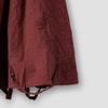 Close-up of Aili cotton pinafore dress in terracotta, showing side hemline button and lace trim detail