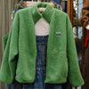 American Vintage green sherpa fleece zip jacket with stand collar, hanging open over denim overalls in the Pomme shop
