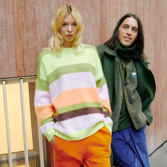 Model wearing an American Vintage Vitow alpaca crew knit in lime, lilac, peach and brown stripes, with orange trousers