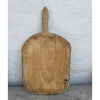 Pale vintage wooden bread board with a pointed handle and worn knife marks, leaning against a whitewashed wall
