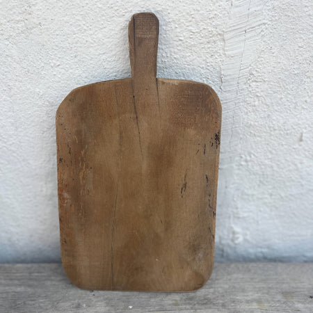 Rectangular vintage wooden bread board with a rounded handle, leaning against a whitewashed wall