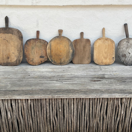 Six vintage wooden bread boards in different shapes and tones lined up on a weathered timber bench