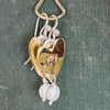 Close-up of a Flick Pope brass heart earring with a white pearl drop