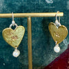 Flick Pope brass heart pearl drop earrings on a gold stand, green backdrop