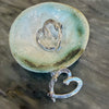 Flick Pope Cross Your Heart silver stud earring, single, on a ceramic dish