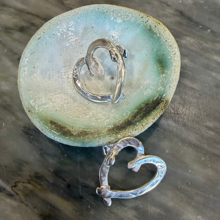 Flick Pope Cross Your Heart silver stud earring, single, on a ceramic dish