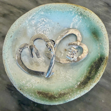 Flick Pope Cross Your Heart silver stud earrings on a ceramic dish