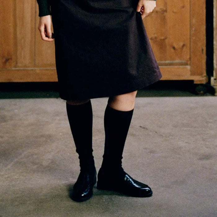 Model wearing Francie tip toe knee-high socks in black, styled with a black dress and loafers