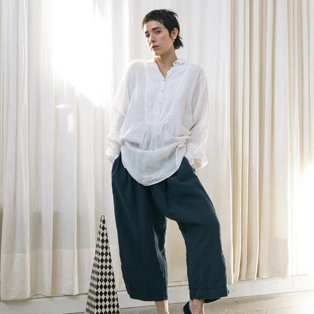 Model wearing the Françoise French shirt in white European linen with a minimal collar and gathered bib front, styled with navy wide-leg linen pants
