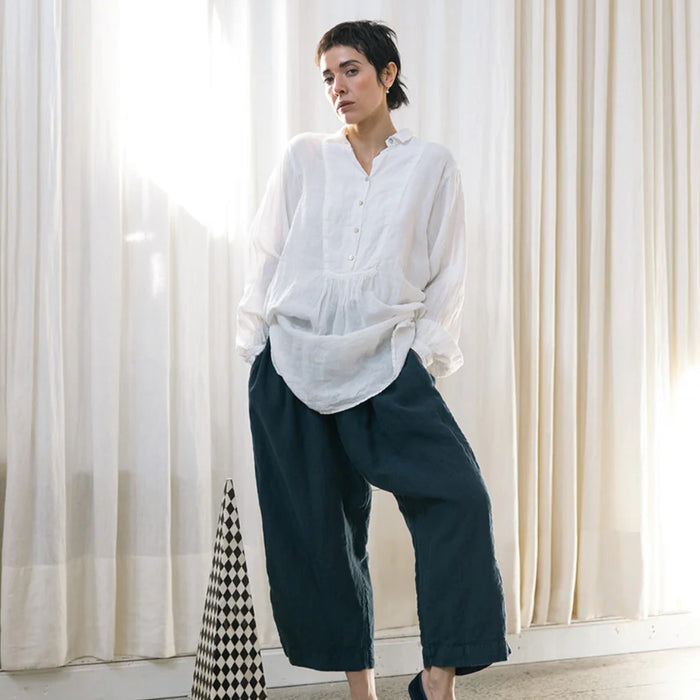 Model wearing the Françoise French shirt in white European linen with a minimal collar and gathered bib front, styled with navy wide-leg linen pants