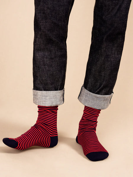 Red and navy striped socks worn with dark jeans on a beige background