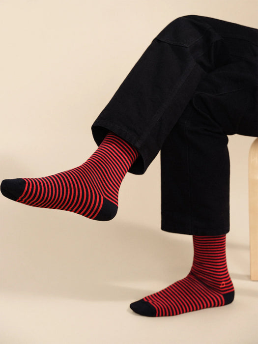Person wearing navy and red striped socks with black pants on a beige background