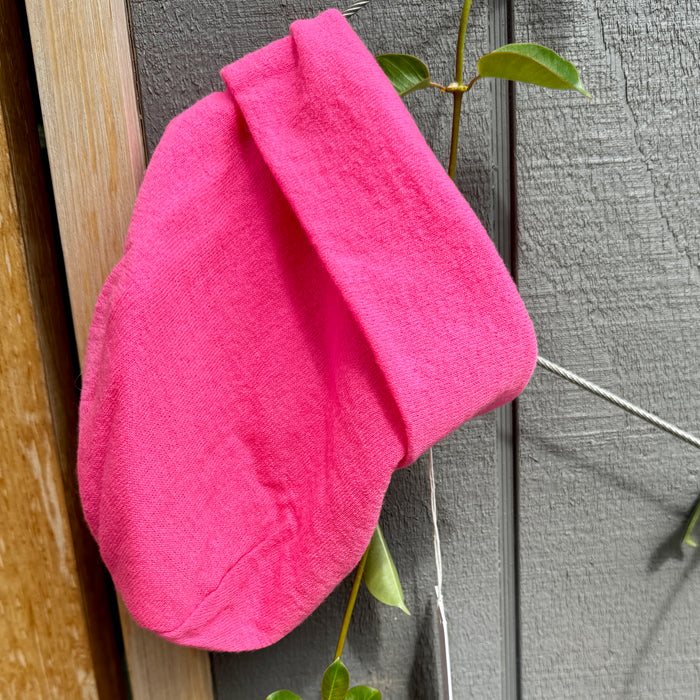 Manuelle Guibal Pepe fine knit beanie in fluoro pink, hung on a garden fence