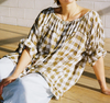 Metta Melbourne Gabrielle gathered blouse in olive check, worn seated on a timber floor