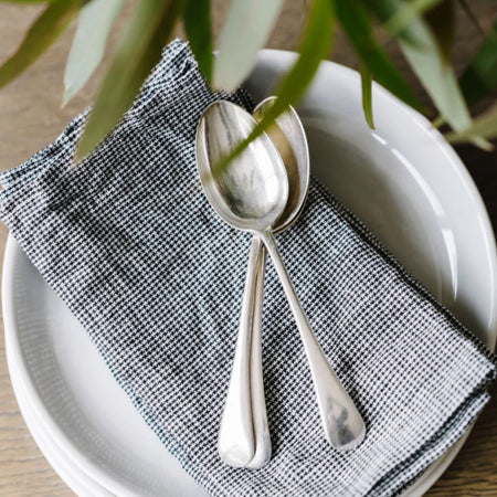 Metta Melbourne black houndstooth linen napkin set on a white plate with silver spoons