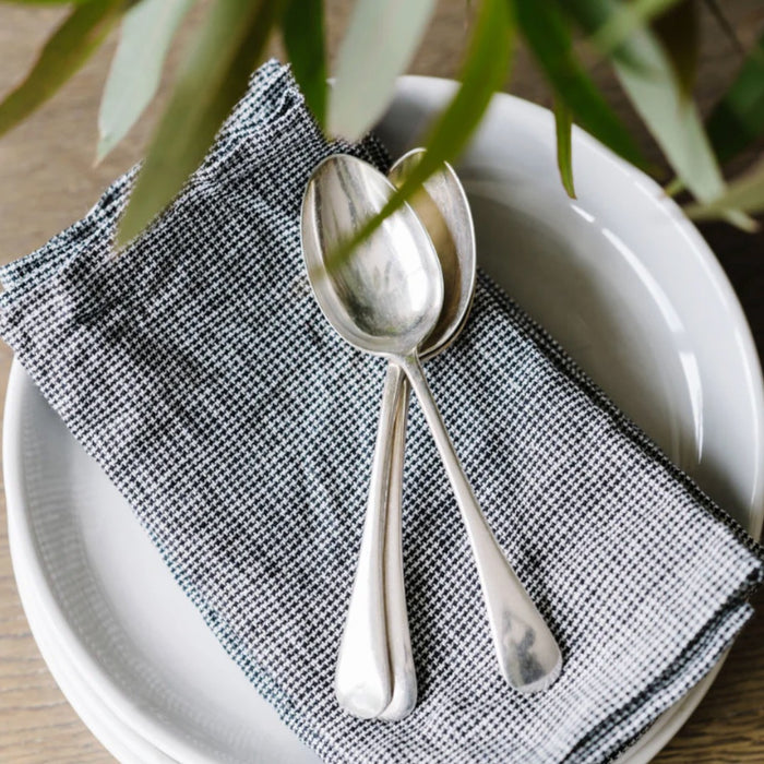 Metta Melbourne black houndstooth linen napkin set on a white plate with silver spoons
