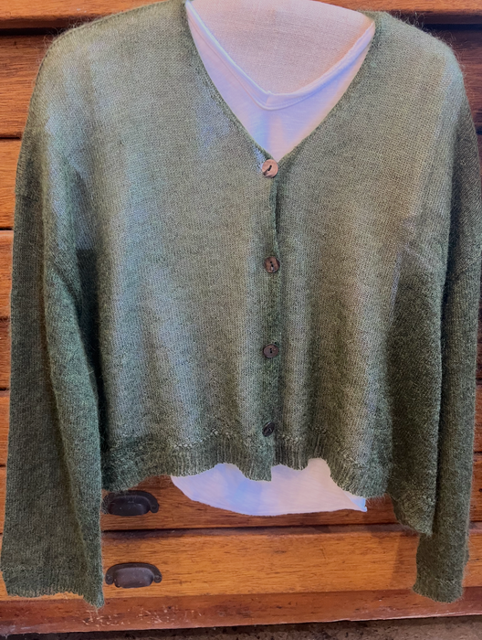 Green cardigan on a mannequin with a white shirt underneath against a wooden background