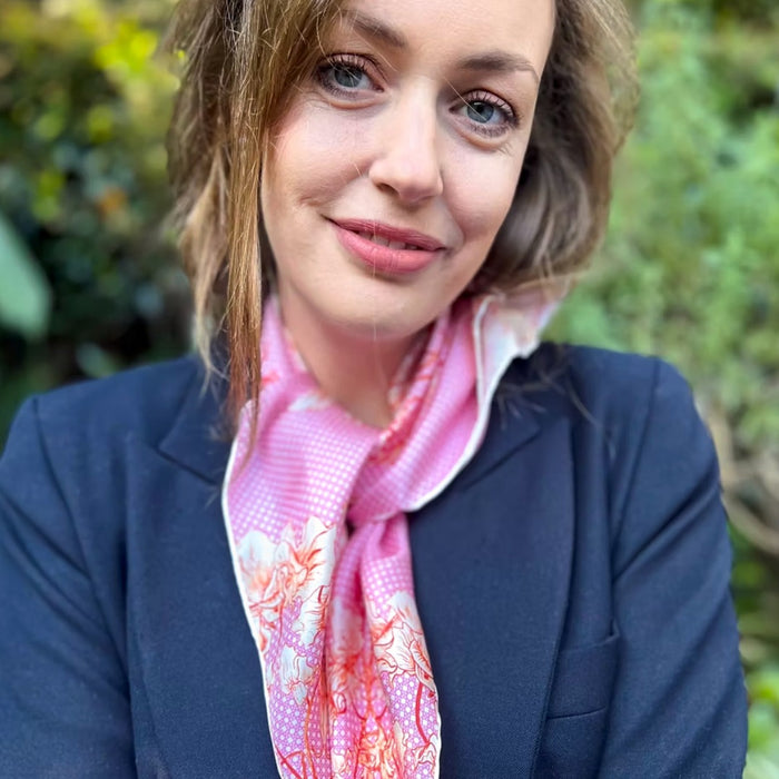 Woman wearing the Oliver Wilkinson Dancers pink silk scarf tied at the neck with a navy blazer