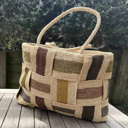 Woven raffia bag with a patchwork pattern on a wooden surface