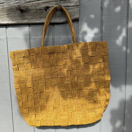 Sophie Digard mustard woven XL raffia tote bag hanging on a timber wall