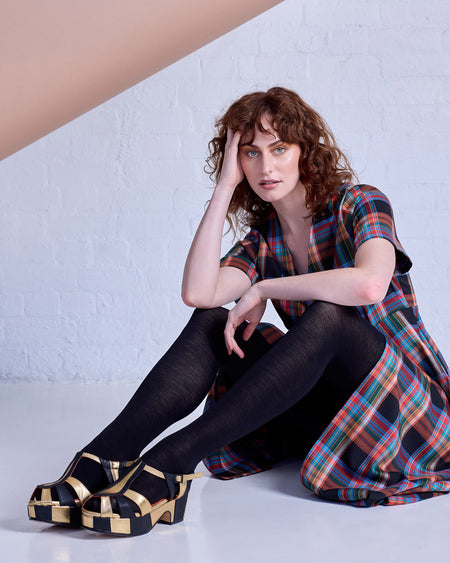 Model wearing Tightology Luxe black merino wool tights with tartan dress and gold platform sandals
