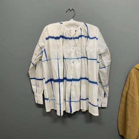 White shirt with blue stripes on a hanger against a gray wall