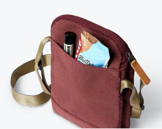 Bellroy City Pouch in plum, front pocket packed with sunglasses and a face mask